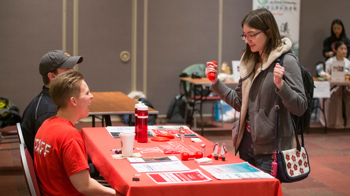 Student at a table during the Stress Less Day event, engaging with two students sitting behind the table.