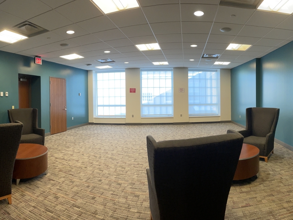 Open room with blue walls, three large windows, and 4 armchairs with coffee tables between them.