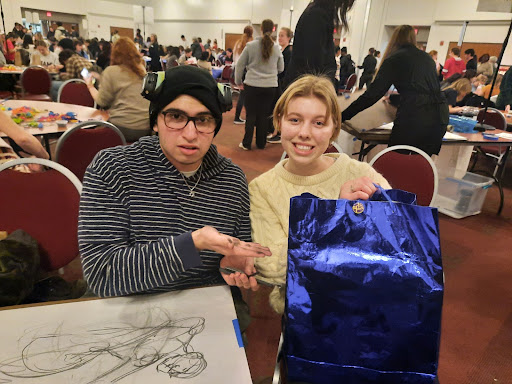 Miriam Woodward with her friend, sitting at a charcoal art table at Art After Dark. Miriam is holding a large blue gift bag.