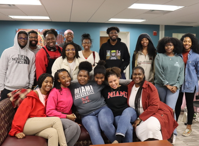 Group of 16 Black students, mostly in Miami gear, smiling and posing in the C-Suite of Armstrong