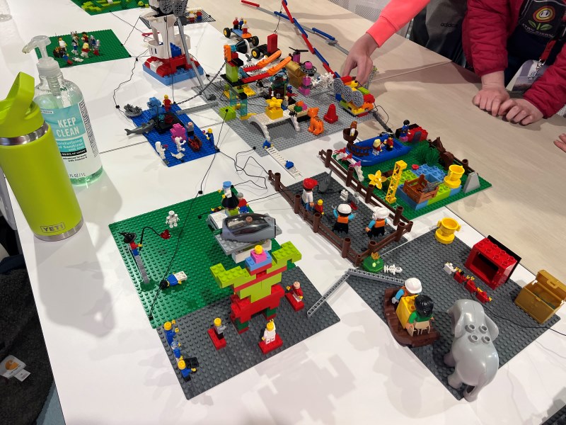 Closeup of seven different lego builds of people, structure, and animals. All the builds are connected with string or connection bricks. 
