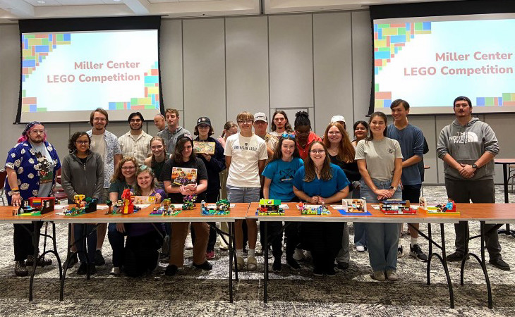 Group of about 25 students posing behind a long table of about 10 separate lego builds
