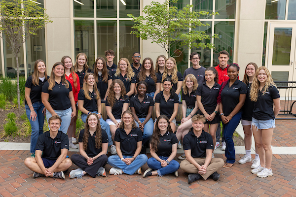 Group of about 25 students in mostly black or red shirts, posing outside the clinical health sciences building.