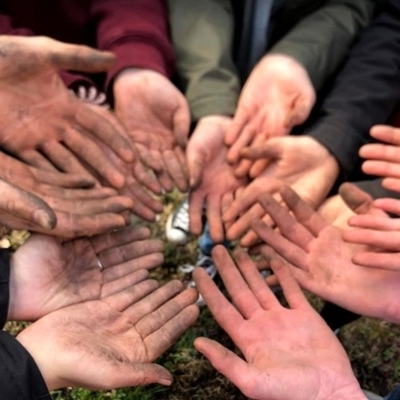 About 10 pairs of hands covered in mud
