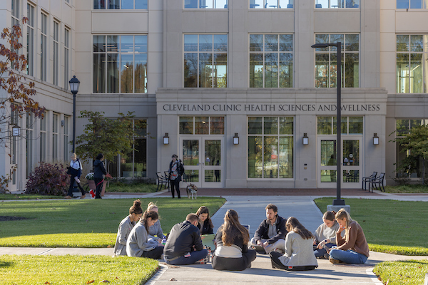 Students sitting on the sidewalk in a circle outside of the Cleveland Clinic Health Sciences and Wellness facility