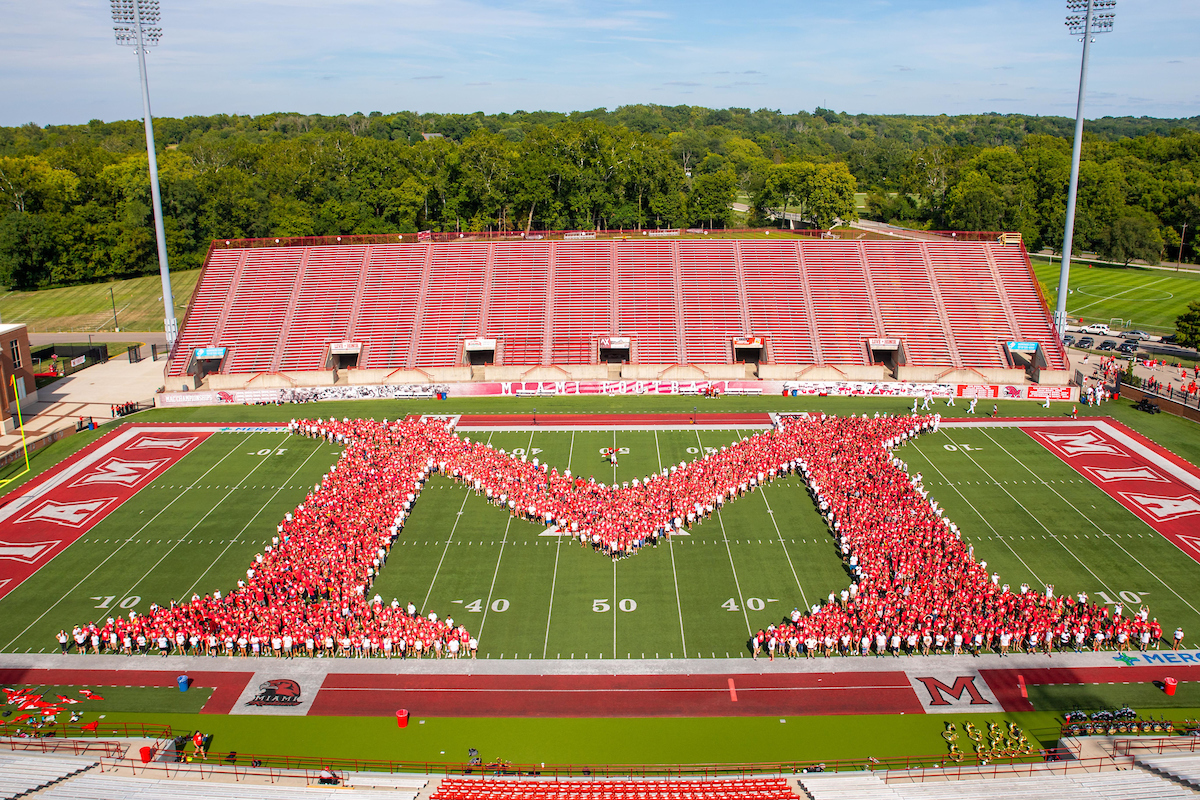 Students dressed in red t-shirts form a giant M on the football field.