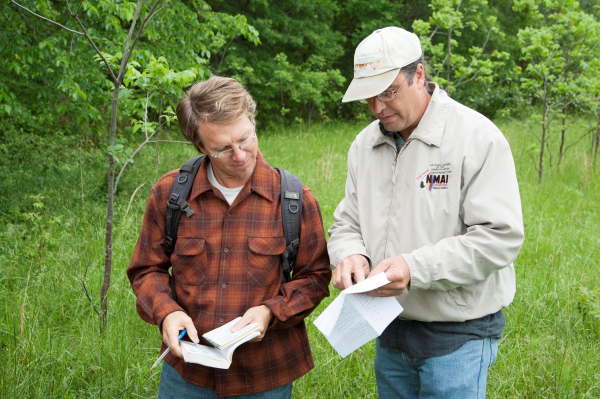 Daryl Baldwin, executive director of the Myaamia Center, and Michael Gonella conduct field research together in a grassy tree lined field.