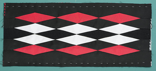 Sample of myaamia ribbonwork of a black fabric rectangle with an alternating pattern of red and white diamonds