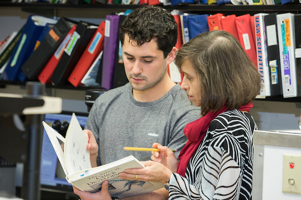A student and advisor look at a book together.