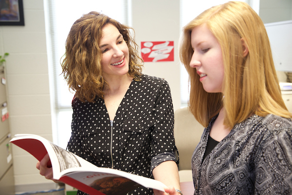 A student and advisor look at a book together.
