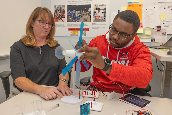 A student and advisor look at a windmill model together.
