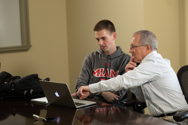 A student and advisor look at a computer together.