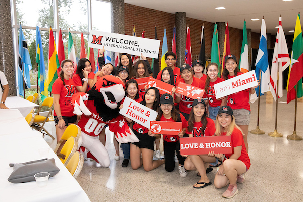 A group of students and Swoop pose with a "Welcome International Students" sign.