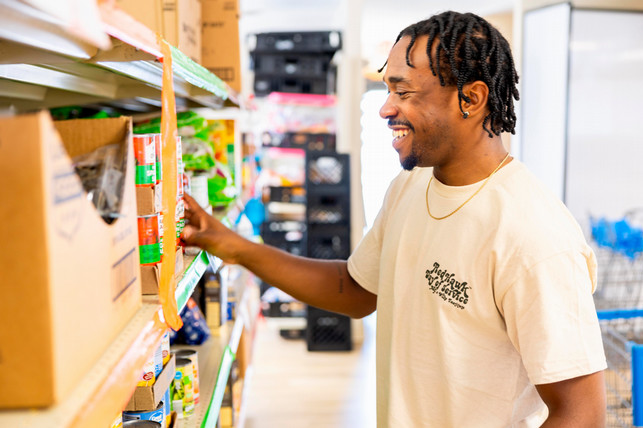 A student standing at a shelf in the local food pantry picking out a can good.