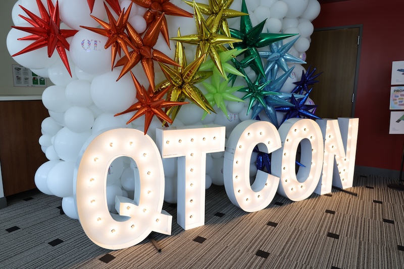Staff in rainbow attire posing by light up letters that read QT-Con.