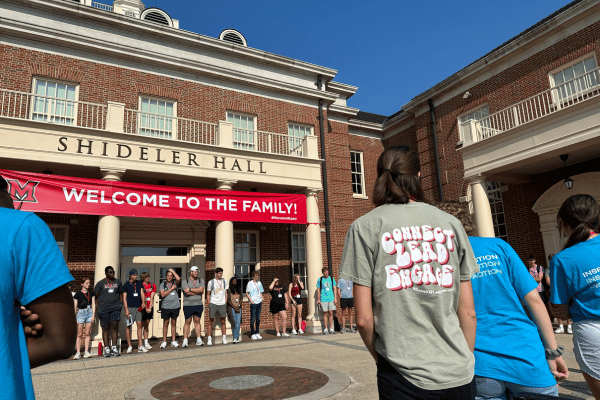 large group of students in a circle around the front of Shideler Hall. A banner hanging on the front of the building reads Welcome to the Family!