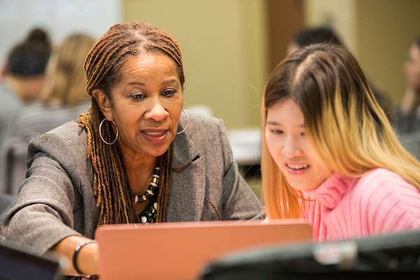 La profesora Paula Saine trabaja en estrecha colaboración con un estudiante en su clase y miran juntos una computadora portátil.