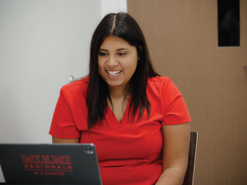 A smiling Miami student looking at their laptop computer