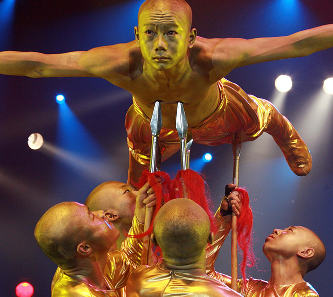 Chinese acrobat balancing on spears held by additional performers