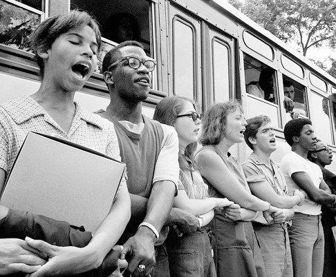 Students holding hands and singing in front of freedom summer bus
