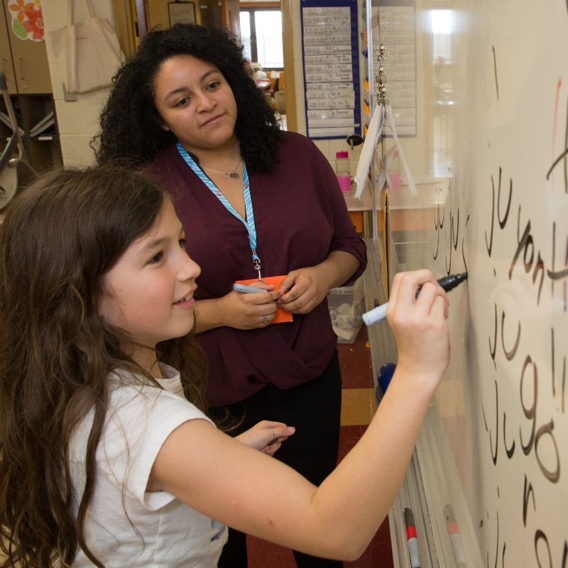 teacher teaching a young student a foreign language on a white board