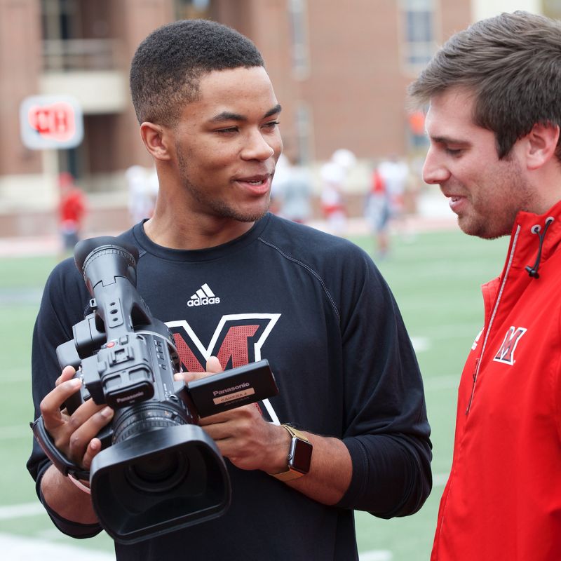 student with a video camera on a football field
