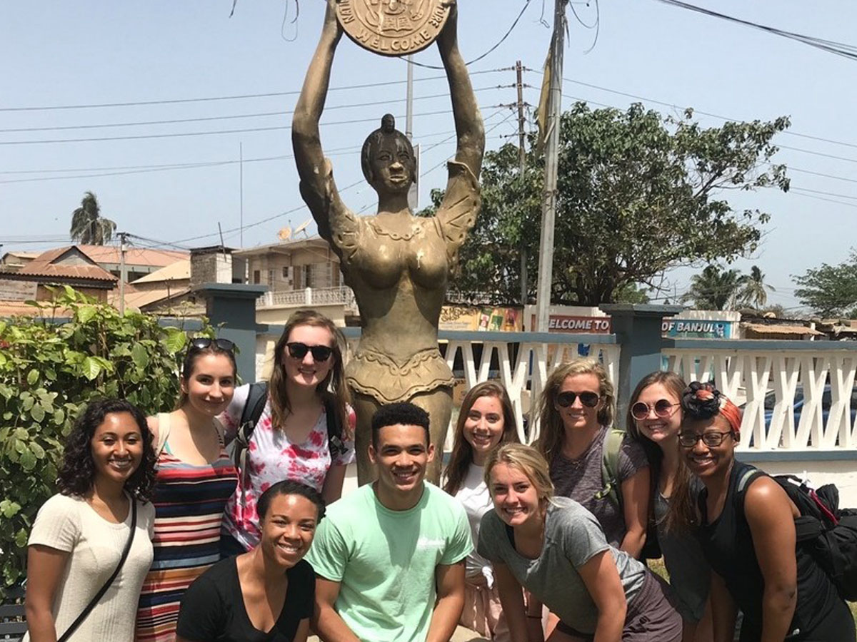 Student group posing next to a bronze statue of a woman holding up a large disk