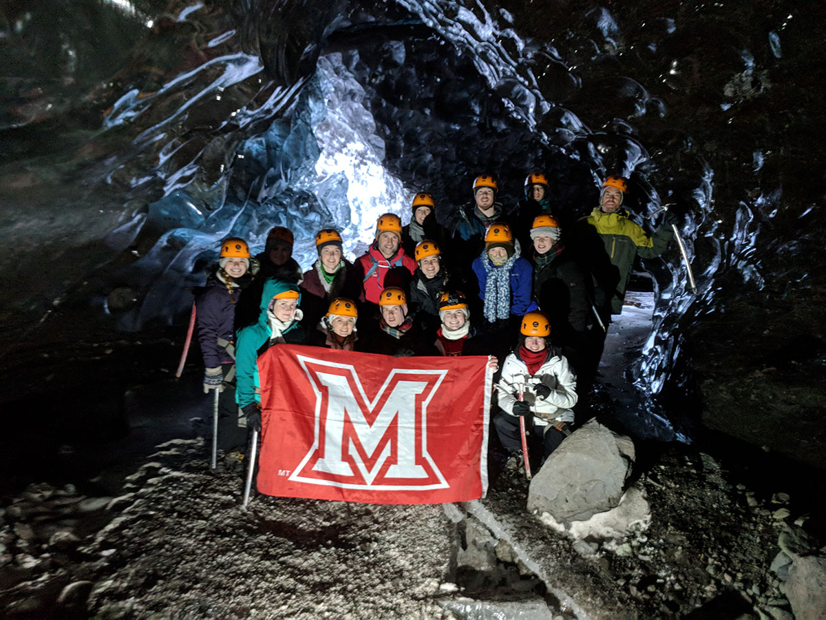 Students posing with a Miami flag while inside a deep blue glacial cave