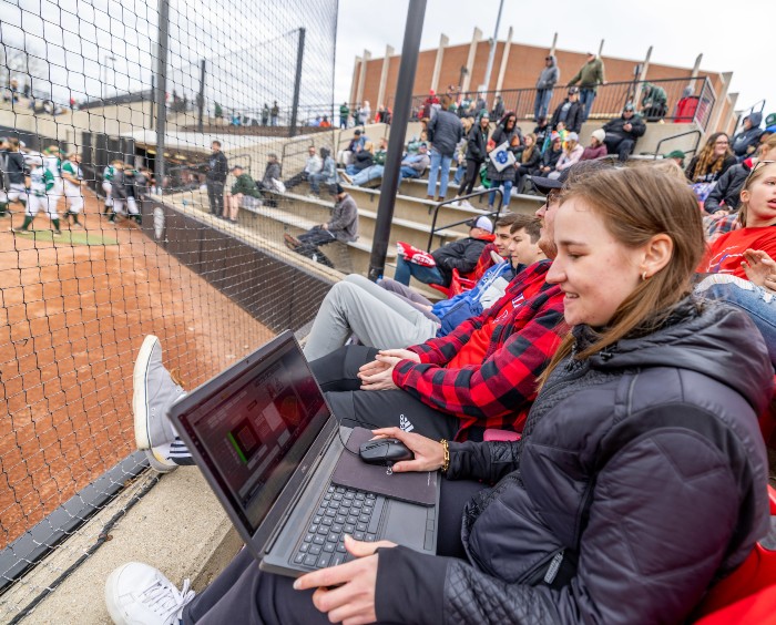 Caroline Brega, sitting at a baseball game with her laptop keep track of the game's analytics