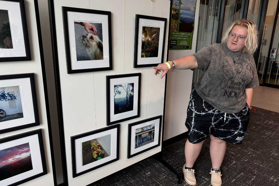Mel Hale gestures toward one of their framed photographs in the Pura Vida: Education and Community in Costa Rica exhibit, displayed in the McVey Data Science Building.