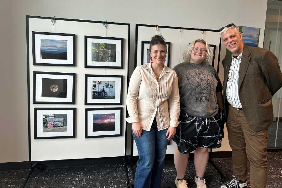Molly Moran, Mel Hale, and Michael Bailey-Van Kuren stand in front of framed photographs from the Pura Vida: Education and Community in Costa Rica student exhibit, displayed on the second floor of McVey Data Science Building.