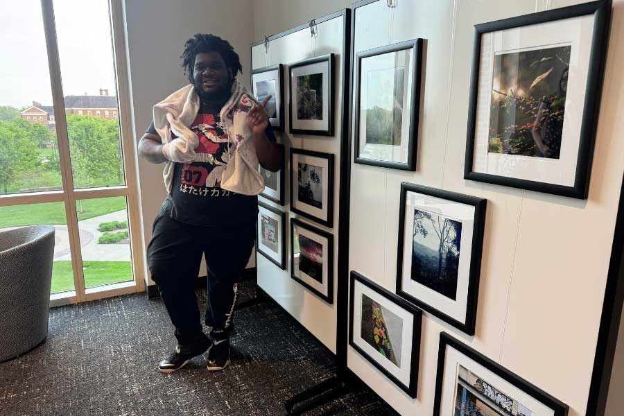 Myles Harrison poses next to framed photographs from the Pura Vida: Education and Community in Costa Rica exhibit in Miami University’s McVey Data Science Building. The exhibit features student photography from a J-Term study abroad program.