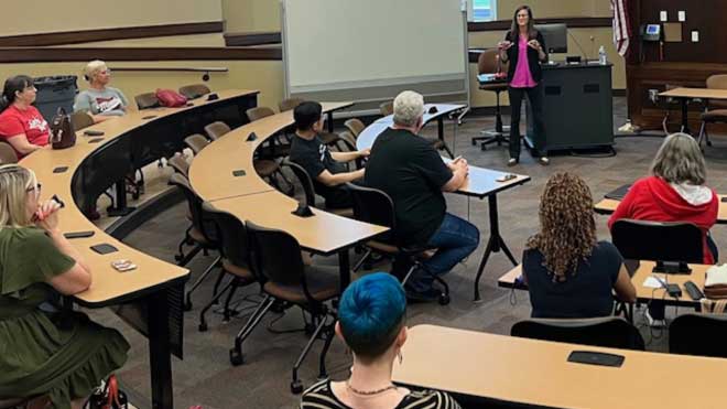EHS Dean Amity Noltemeyer speaks at a podium to a seated audience in a curved lecture hall. Attendees listen attentively during the presentation.
