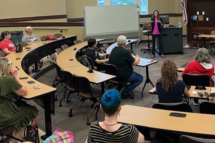 EHS Dean Amity Noltemeyer speaks at a podium to a seated audience in a curved lecture hall. Attendees listen attentively during the presentation.