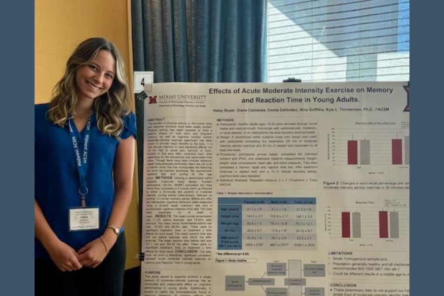 Miami University student standing next to a research poster on exercise, memory, and reaction time in young adults.