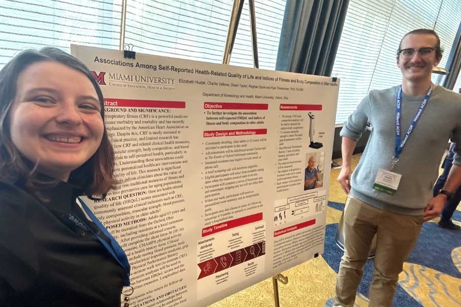 Two Miami University students presenting research on health-related quality of life in front of an academic poster.