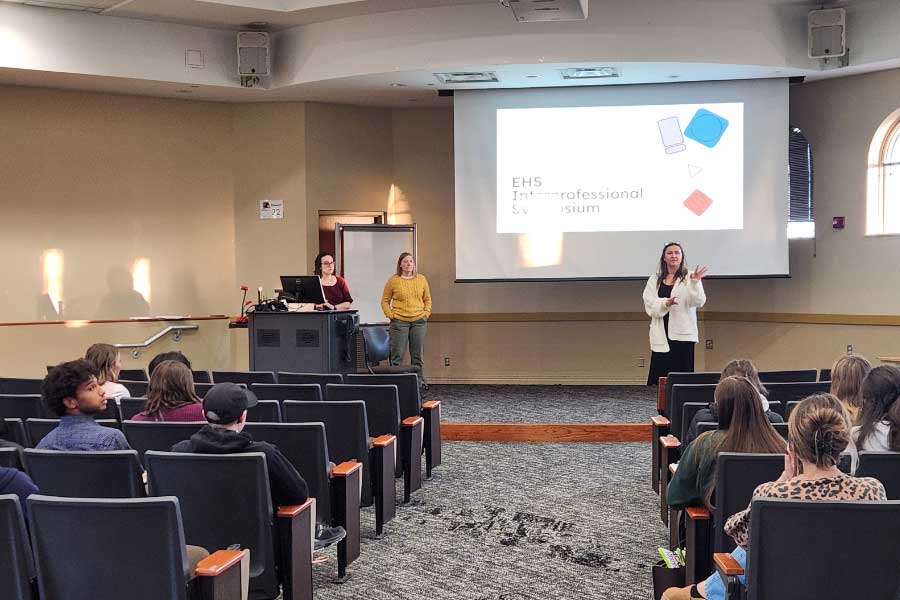Faculty present at the EHS Interprofessional Symposium while students listen in a lecture hall.