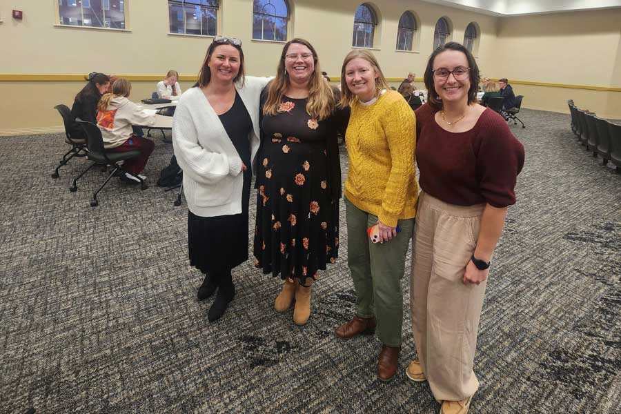 Four women pose together in a conference room during the EHS Interprofessional Symposium.