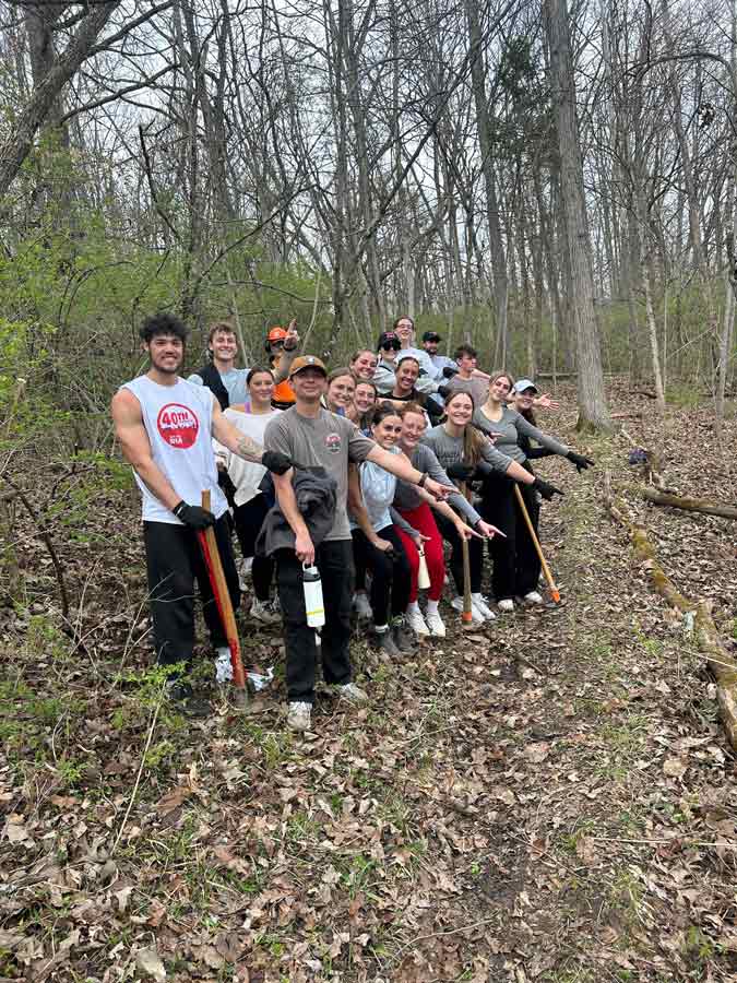 KNH 402 Capstone class standing together pointing downward at a tree they chopped down at Heuston Woods.