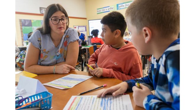 An EHS student teacher works through reading comprehension sheets with students at Hamilton City Schools.