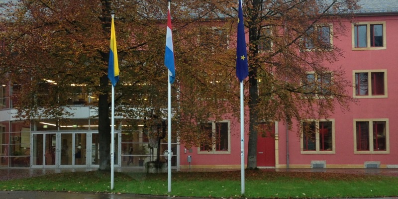 Image of the front of Luxembourg school building with three flagpoles in the foreground.