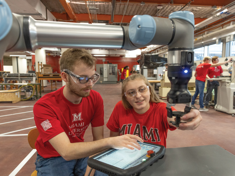 2 Engineering Technology students using a tablet to control a robot arm. 