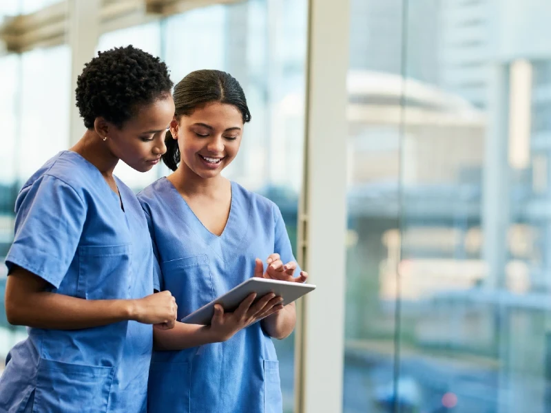 two nurses in blue scrubs looking at i pad in hospital