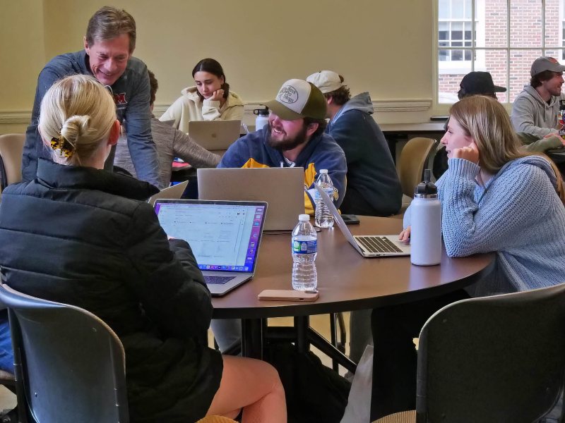 professor Mark Lacker talking with group of student sitting at a round table in classroom