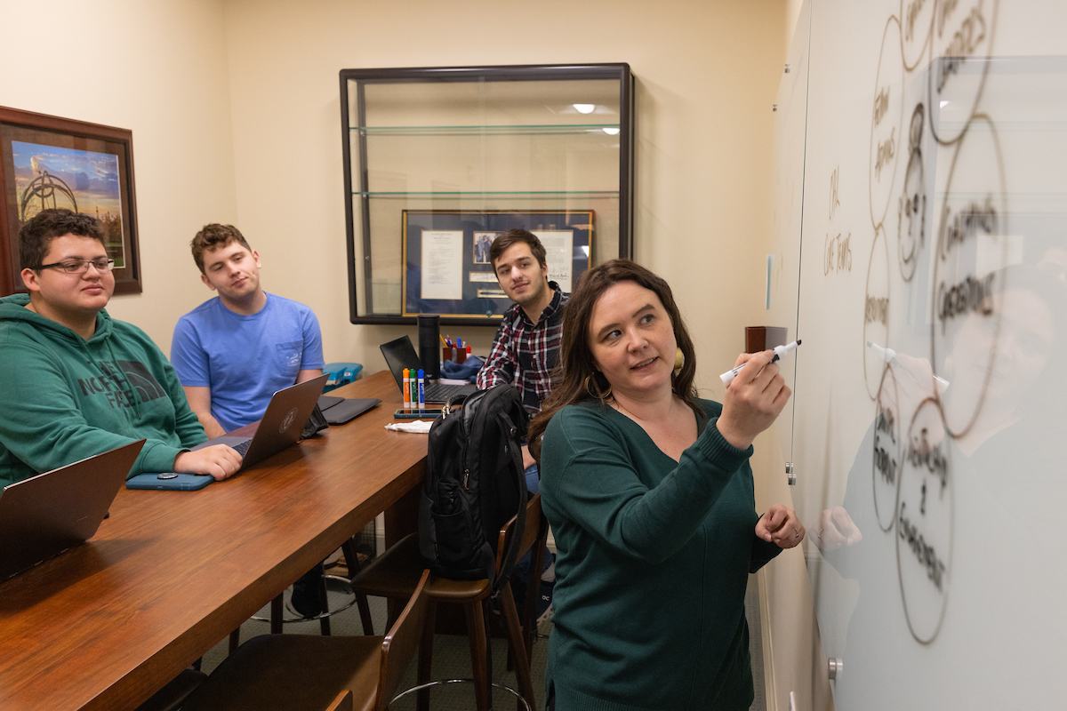 professor Megan Gerhardt writing on white board with group of students in a classroom