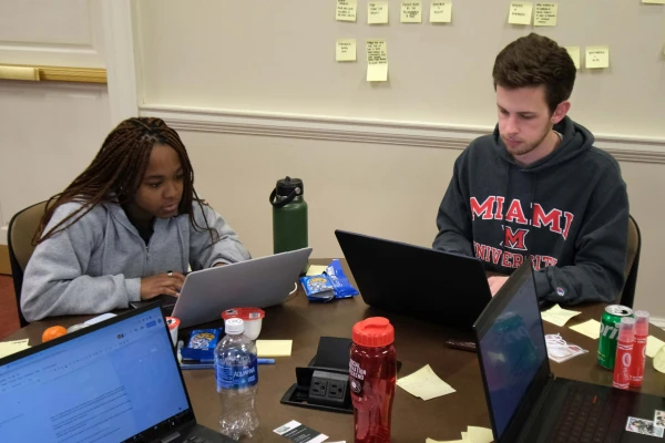 two students working at desk with laptops during social innovation weekend