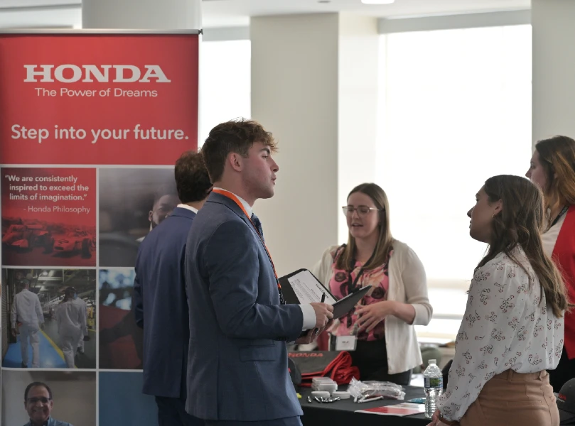 student talking with a Honda recruiter at event with Honda poster in backgroun
