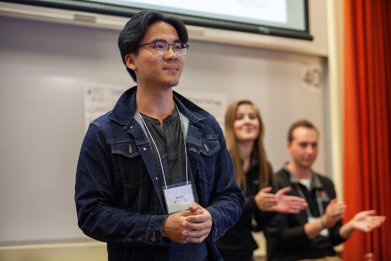 Miami student smiles in front of his class that he just gave a successful presentation to. Fellow students applaud behind him.