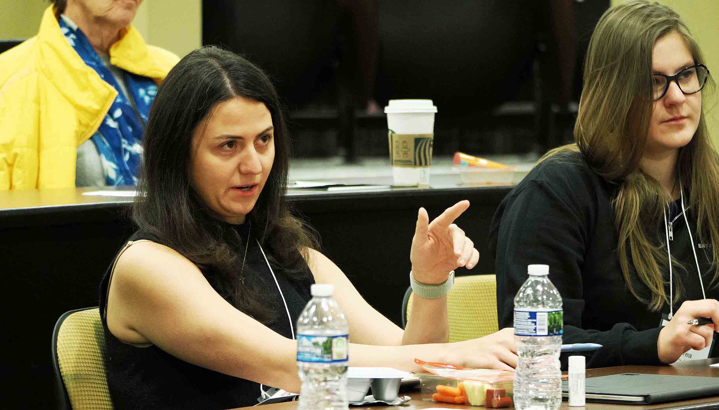 Two women seated at a conference table during a workshop, with one gesturing while speaking.