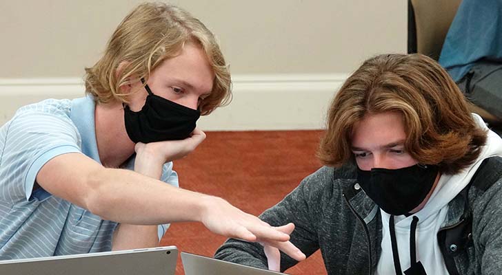 Student points at another student's laptop screen